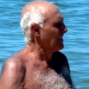 Elderly balding man with white hair, standing shirtless in a body of blue water